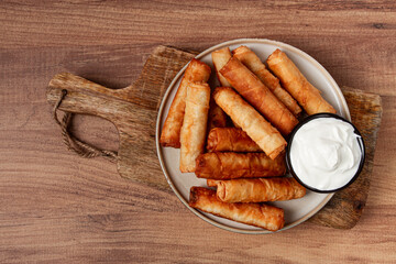 fried spring rolls with cheese, on a wooden background, with cream sauce, no people,