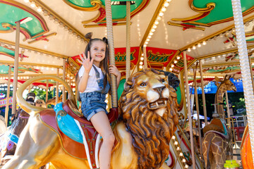 Happy emotional child riding on a merry go round at amusement park. Little girl playing on...