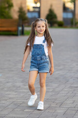 Fototapeta premium Smiling little girl is having fun walking down the street. Urban lifestyle concept. City background.