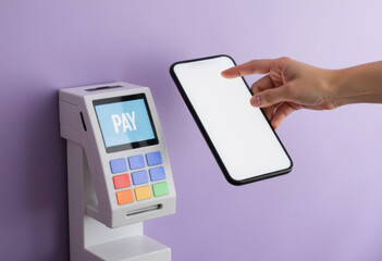 Hand holding smartphone near payment terminal on purple background