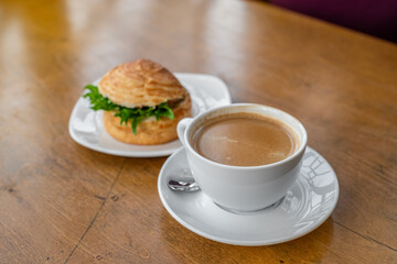 Top view of a breakfast scene featuring a flaky croissant sandwich filled with fresh greens and paired with a steaming cup of rich café crema. Cozy and elegant breakfast concept.
