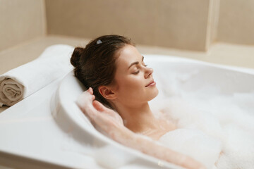 Naklejka premium Relaxed young woman enjoying a bubble bath in a modern bathroom, surrounded by soft lighting and neutral colors. Wellness and self-care concept emphasized.
