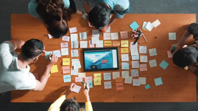 Top down view of programmer brainstorming and planning about web design while looking at tablet wireframe prototype. Aerial view of skilled developer team talking about digital application. Symposium.