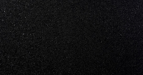 A top-view black sandpaper texture background featuring a grainy, rough surface with black glitter dust subtly floating in the air. The combination of matte and sparkling elements creates depth and a 