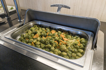 Many of boiled brussel sprouts with carrot slices as garnish and side dish. Vegetables vegan food for service in hotels and hostels