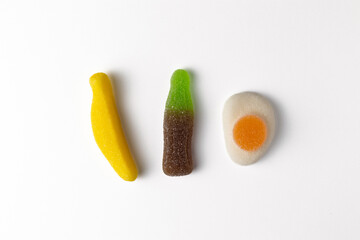 Colorful gummy candies representing banana, soda bottle, and fried egg on white background