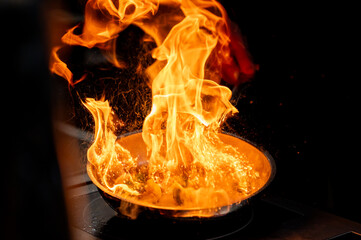 Close-up of a frying pan with high flames, depicting a dramatic cooking scene. Perfect for culinary...