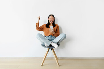 Yes. Excited woman celebrating win and success, using cellphone and shaking clenched fist, reading...