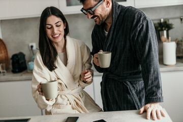 Happy couple wearing bathrobes drinking coffee in kitchen