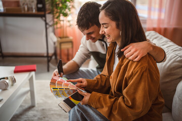 young couple holding color swatches at home while sit on sofa at home