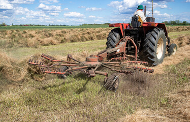 Farmer using a tractor to rake hay in open field on sunny day