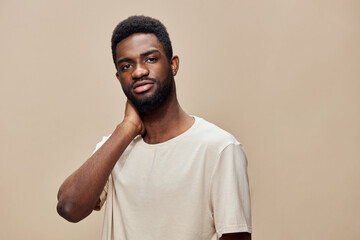 Confident young man with dark skin, wearing a casual beige t shirt, showcasing a thoughtful expression against a warm neutral background