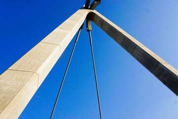 Obraz premium Emporragender Brückenpfeiler aus Beton mit Kabelseil vor blauem Himmel bei Sonne am Nachmittag im Sommer