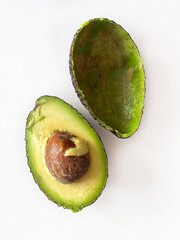 Ripe green avocado cut in half on white background, close-up, top view. One half is whole with a round brown pit, the other is empty, only the peel. Healthy eating.