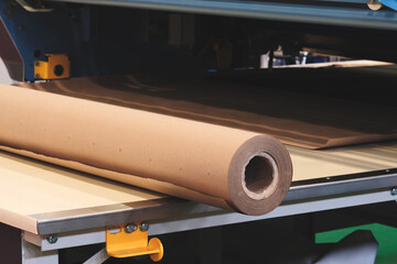 A roll of brown paper is being fed into a machine. The roll of paper is being cut into smaller...