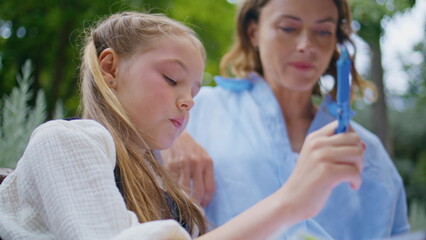 Closeup pensive schoolgirl writing copybook with mom at park. Kid holding pen