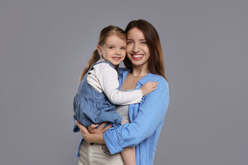 Portrait of happy mother with her cute little daughter on grey background