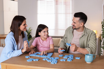 Fototapeta premium Happy parents and their daughter solving puzzle together at wooden table indoors