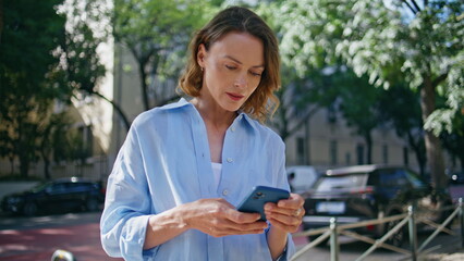 Waiting woman using smartphone at sunny alley closeup. Lady looking distance