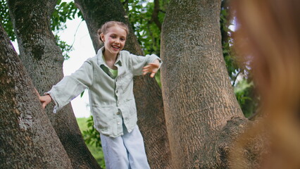Small girl climbing tree walking at green forest. Cute funny child waving hand