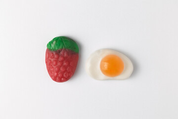 Gummy candy strawberry and fried egg on white background