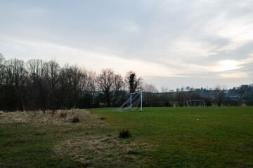 Eham A soccer field with a goal and a few trees in the background. The sky is cloudy and the sun is setting