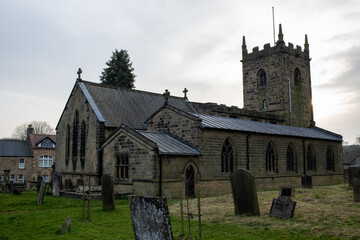 Eham, Chesterfield, United Kingdom - 21 Mar 2025 - Eham Parish church with a cemetery in front of it. The cemetery is full of headstones and the church is surrounded by trees. The sky is cloudy and th