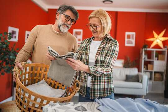 mature couple fold laundry in the living room, domestic life concept - Powered by Adobe