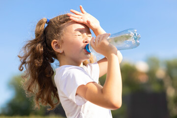 little girl drinking water from bottle in heat. kid suffering from thirst in against blue sky....