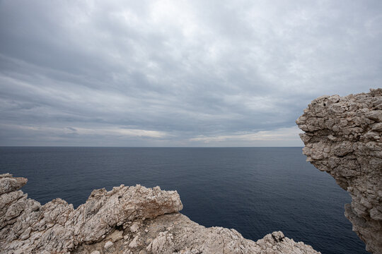 Dramatic view of the Mediterranean Sea from Cape Lefkata, the southernmost point. Rugged white cliffs contrast with the deep blue sea under a cloudy sky, creating a moody coastal landscape.