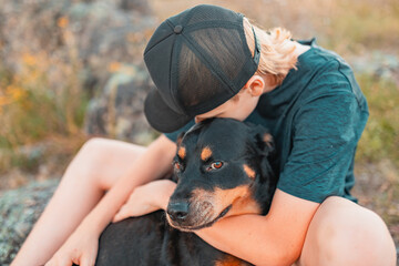Teenage boy and rottweiler dog sitting together on rock in the Australian bush