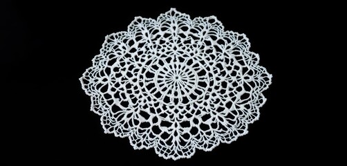 Intricate lacework of a white crocheted doily on a black background, close-up, black, filigree