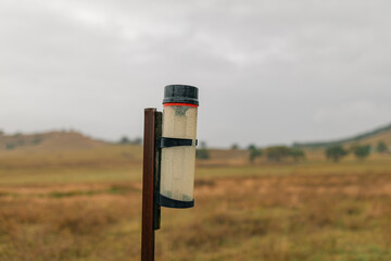 Rain gauge on rural farm property measuring rainfall on stormy day