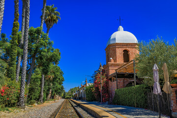 San Juan Capistrano domed bell tower overlooks train tracks framed by palm trees
