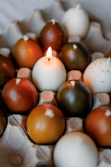 Stylish candles in the shape of painted chicken eggs. Easter theme, Easter egg candles in paper egg trays on a minimalist background, Easter aesthetics
