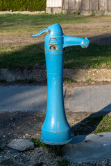 Vintage hungarian blue water pump standing in a grassy area near a pathway during daylight hours