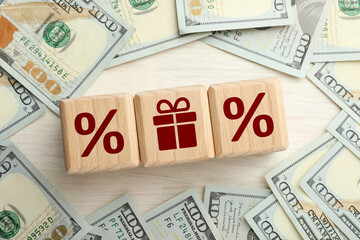 Cube with gift box image among other ones with percent signs and money on wooden table, top view