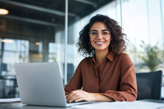 Smiling portrait professional it specialist latin hispanic business lady working on laptop pc sitting in modern office. Young middle eastern indian woman using computer technology for work. Copy space