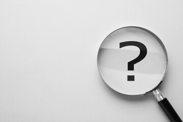 Question mark on light background, top view through magnifying glass. Space for text