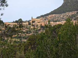 Fototapeta premium Picturesque Valldemossa village view, Serra de Tramuntana mountains, Mallorca, Balearic Islands. Mediterranean buildings, lush greenery, iconic bell tower, traditional terraces, countryside setting.