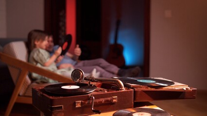 Vintage record player playing a vinyl record with a family relaxing on a sofa in the background, enjoying the music and spending time together