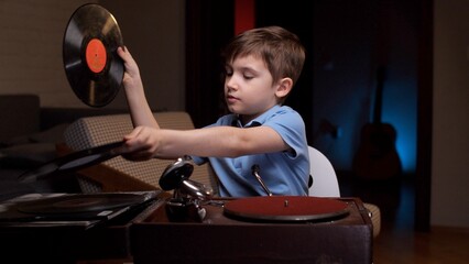 Young boy is choosing a vinyl record to play on a vintage record player. He is concentrating on...