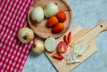 Onions and tomatoes with slices on wood with white background with red checkered cloth decoration
