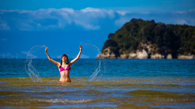 beautiful girl in bikini enjoys a dip in the turquoise water of Abel Tasman National Park, New Zealand South Island; swimming in Stilwell bay with Adele Island in the background