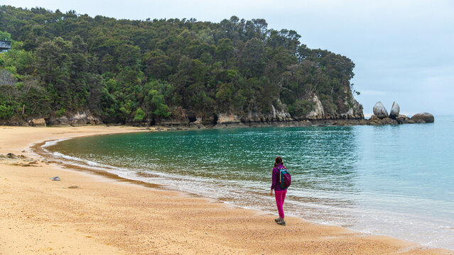 backpacker girl enjoys a walk on the famous beach overlooking split apple rock, unique rock formation in north part of New Zealand South Island near Marahau and Abel Tasman National Park