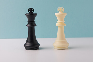 Black and white king chess pieces facing each other on white and light blue background