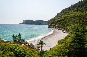 Parc national de ForillonStunning coastal landscape in Gaspésie, Quebec, featuring turquoise waters, a rocky beach, lush green cliffs, and a wooden staircase leading to the shore. A breathtaking natur
