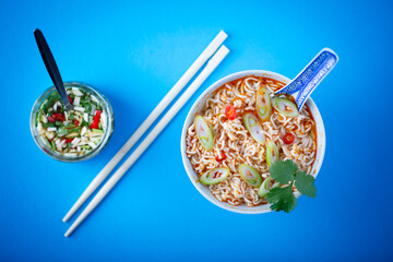 Asian noodle soup with fresh garnish on blue background.
