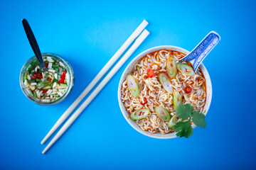 Delicious asian noodle soup with fresh garnish on blue background.