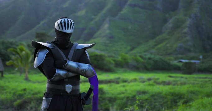 Cinematic tracking shot of ninja in armor posing in front of tropical paradise with purple scarf floating in the wind - medium shot